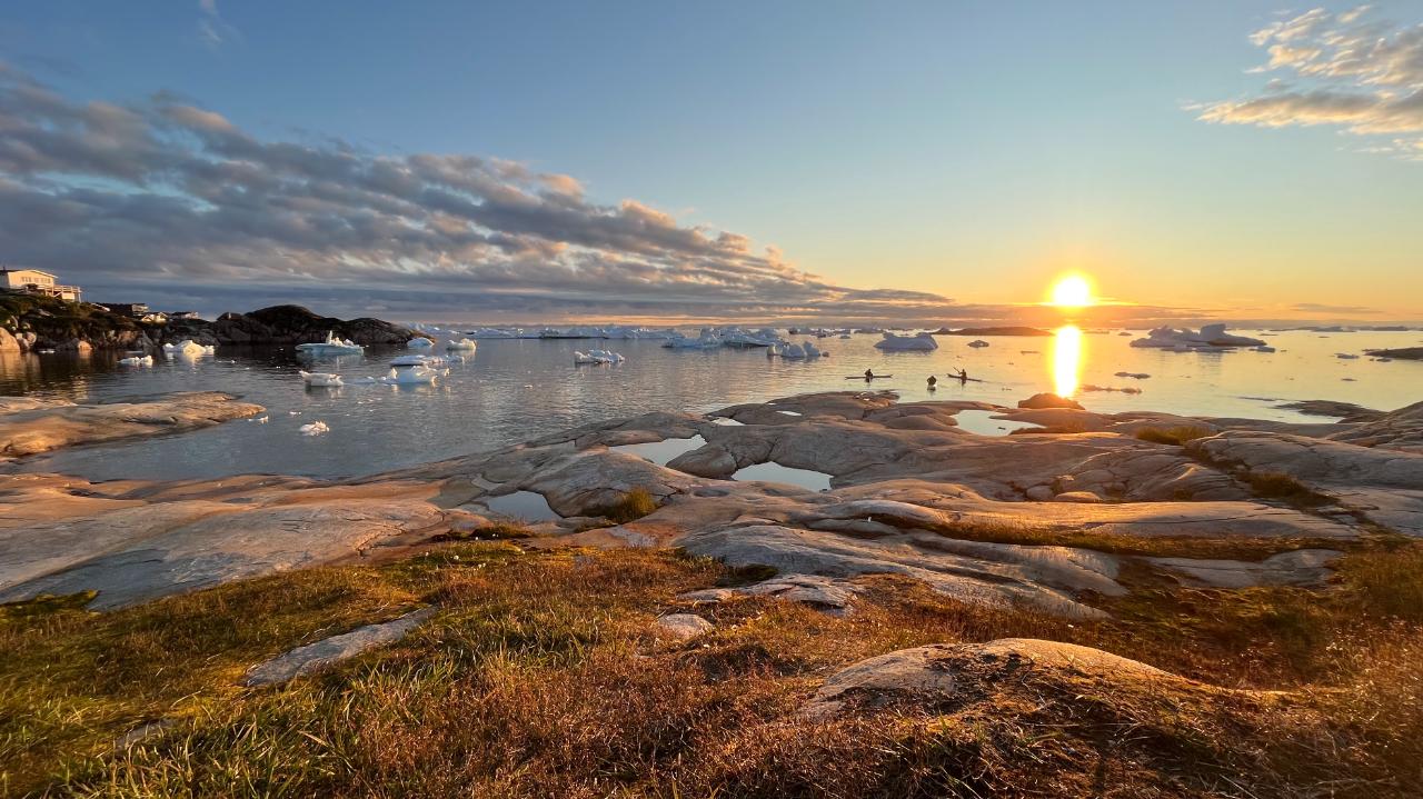 3 people set off in kayaks at sunset in Ilulissat, Greenland.